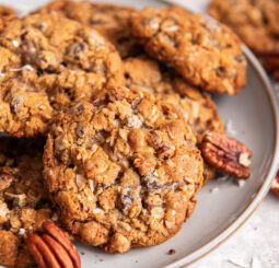 Cowboy cookies on a plate near pecans.