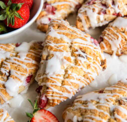 Glazed strawberry scones near a bowl of fresh strawberries.