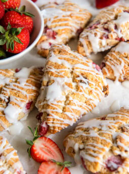 Glazed strawberry scones near a bowl of fresh strawberries.