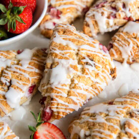Glazed strawberry scones near a bowl of fresh strawberries.