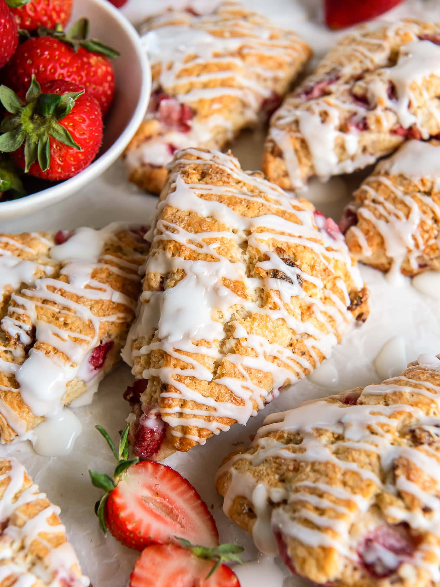 Glazed strawberry scones near a bowl of fresh strawberries.