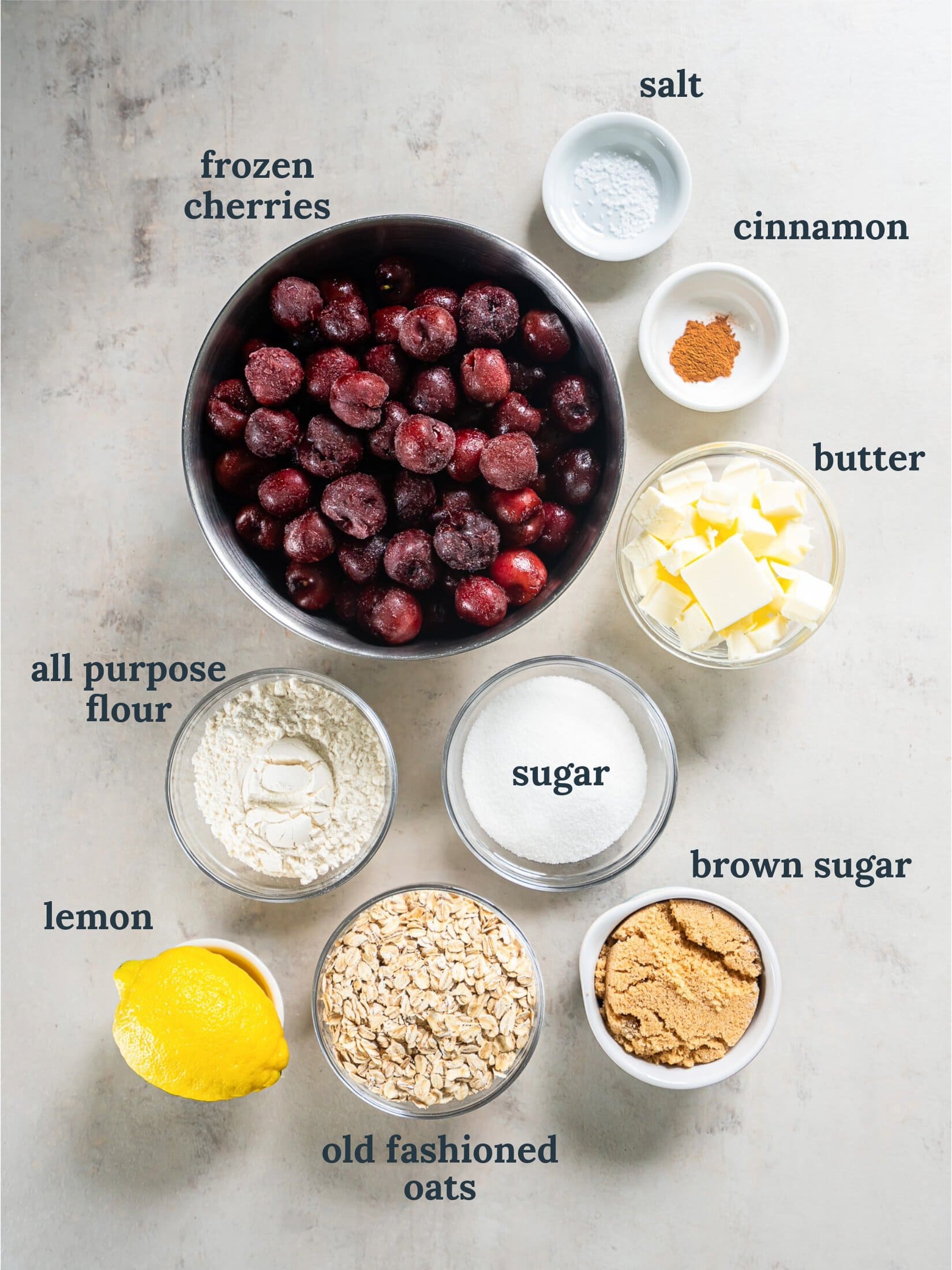 Bowl with frozen cherries near smaller bowls with a lemon, sugar, flour, butter and oats.