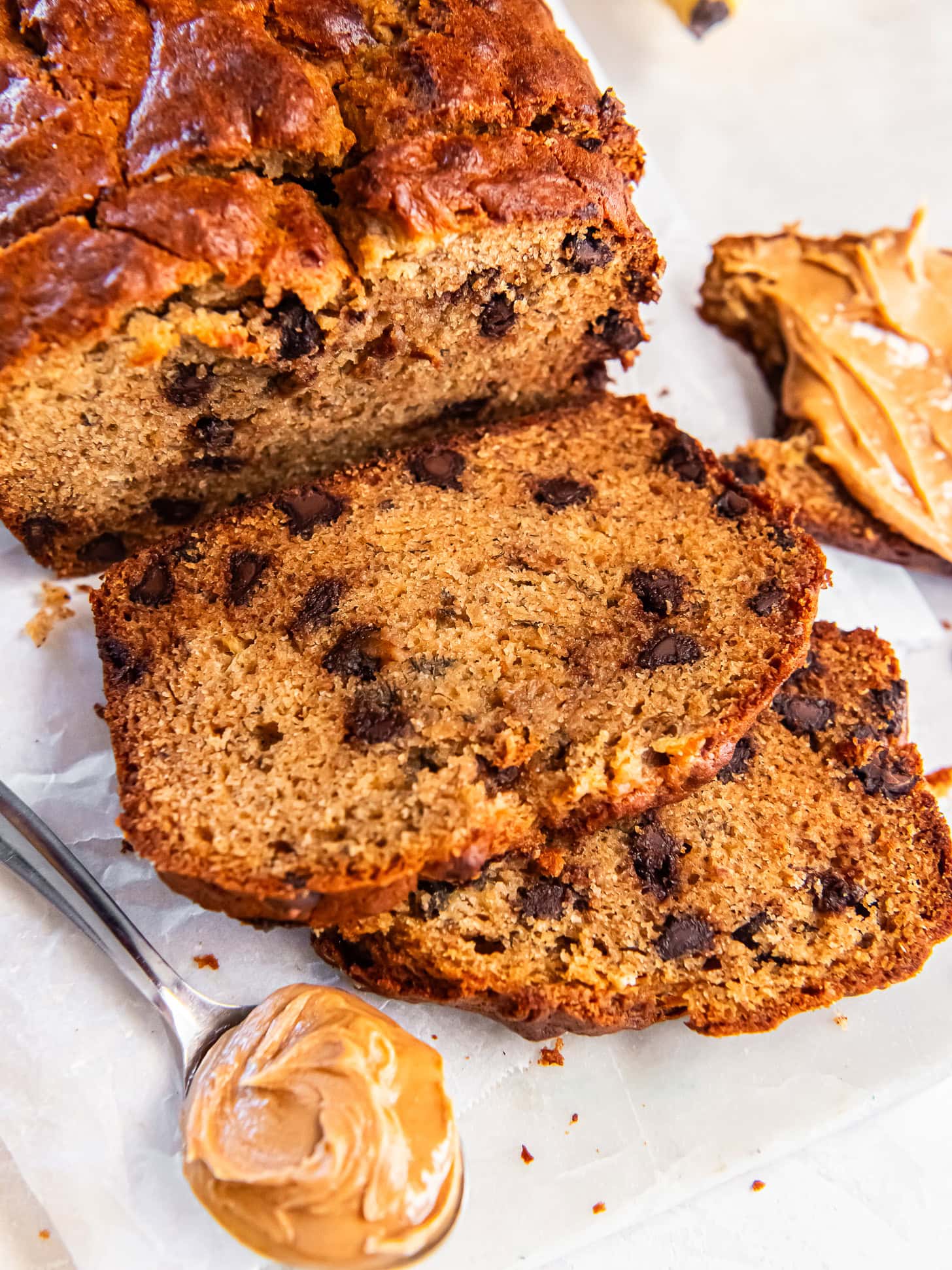 Sliced loaf of peanut butter banana bread near a spoonful of peanut butter.