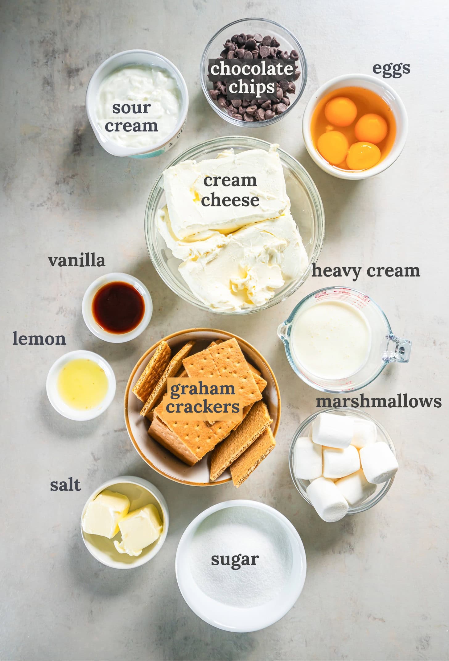 Small bowls with eggs, graham crackers, sour cream, butter, sugar, and cream cheese.