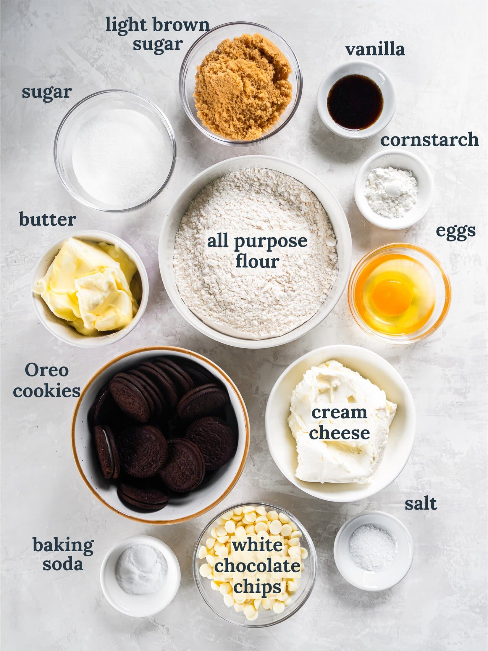 Small bowls with flour, butter, eggs, sugar, vanilla, cream cheese and Oreo cookies.