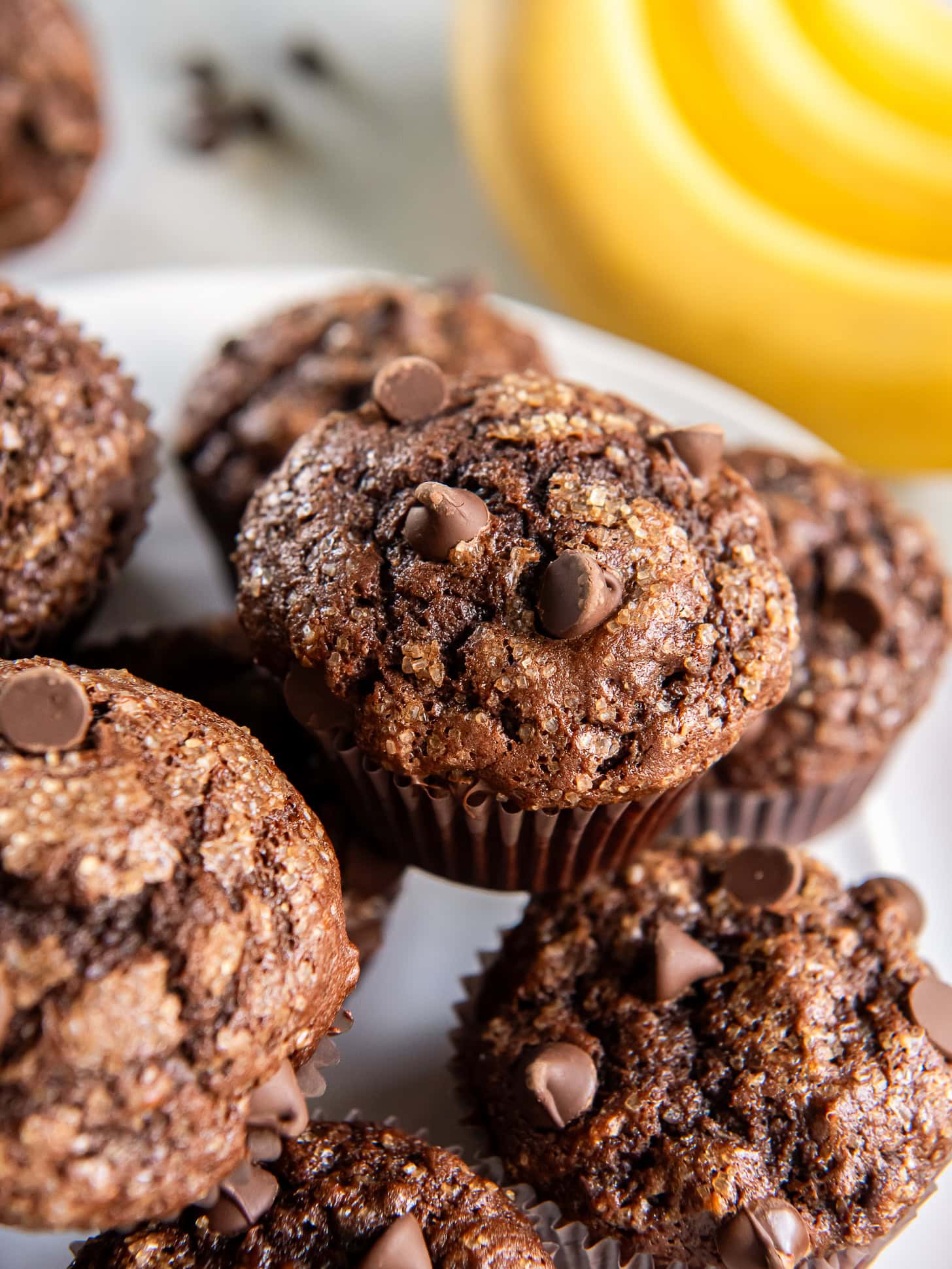 Double chocolate banana muffins stacked on a white plate.