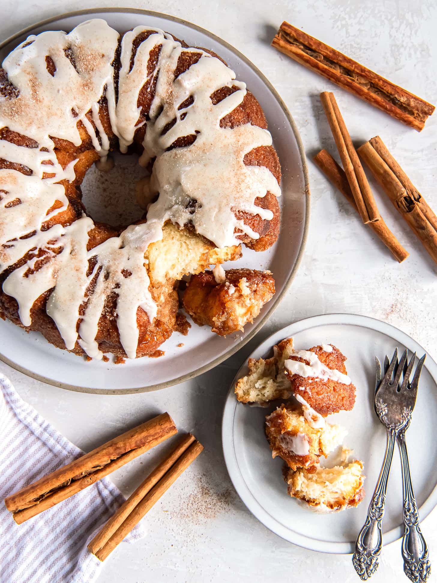 Pull-apart monkey bread served on a white plate near cinnamon sticks.