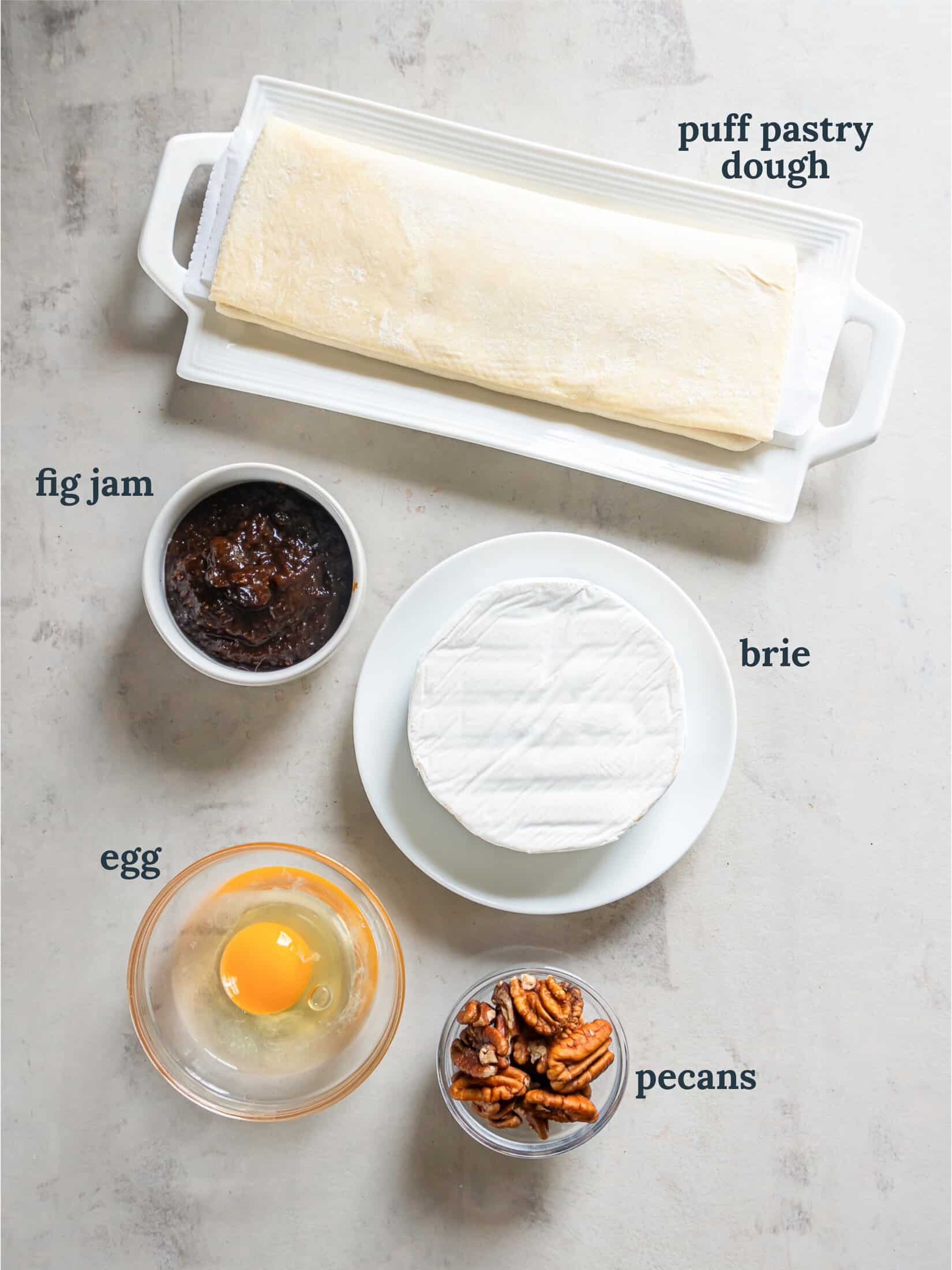 Puff pastry next to brie cheese, fig jam, egg and pecans.