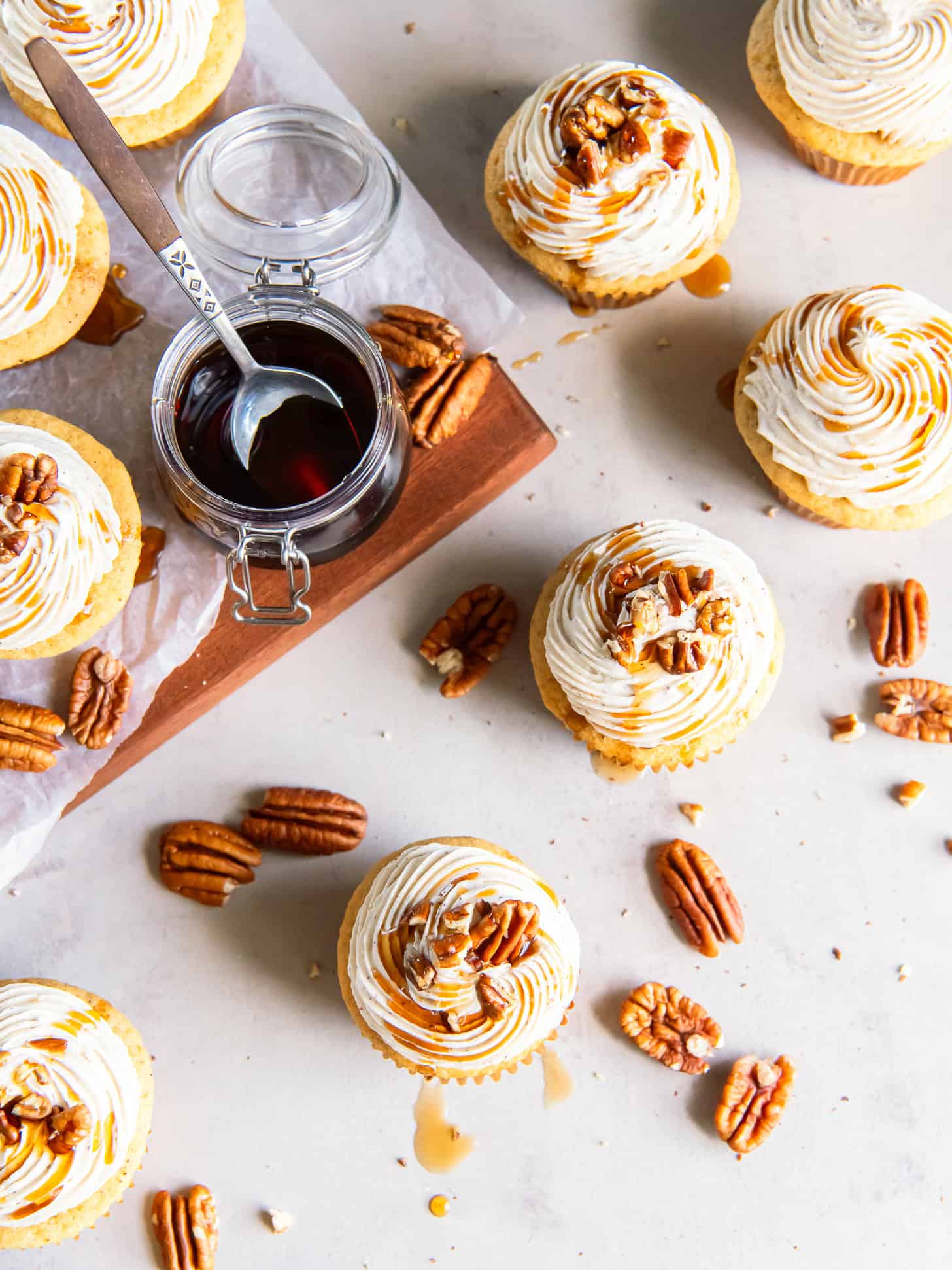 Frosted maple cupcakes with a drizzle of maple syrup and a sprinkle of chopped pecans.
